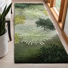 a green rug with white flowers on it in front of a window and potted plant