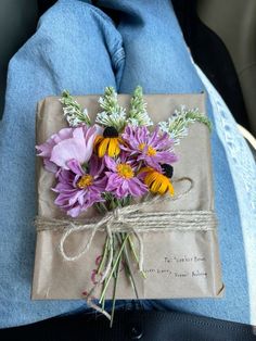 a bouquet of flowers wrapped in brown paper on someone's lap with blue jeans