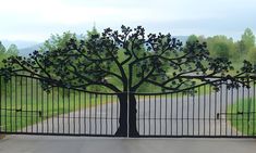 an iron gate with a tree in the middle and a paved road on either side