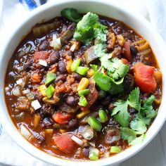 a white bowl filled with chili and vegetables on top of a blue towel next to a spoon