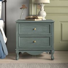 a nightstand with a book and lamp on it next to a bed in a bedroom