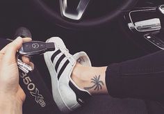 a person with tattoos on their arm holding a cell phone and driving a car steering wheel