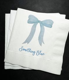 two napkins with blue bows on them sitting next to each other, one has something blue written on it