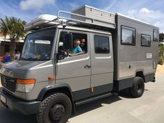 two people are sitting in the driver's seat of a gray truck with an awning