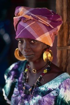 a woman in a colorful dress and headdress poses for the camera with earrings on her ear