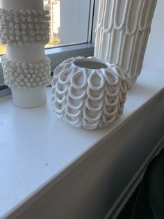 three white vases sitting on top of a window sill next to each other