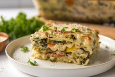 a white plate topped with lasagna covered in cheese and vegetables next to parsley