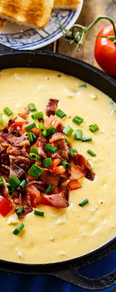 a bowl of soup with bacon and green onions in it on a plate next to bread