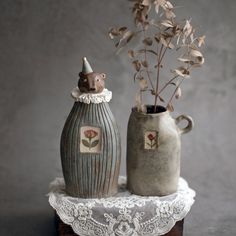 two ceramic vases with flowers in them on a lace doily table cloth,