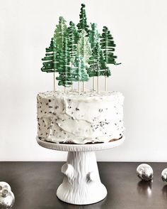 a cake with white frosting and green trees on top is sitting on a table