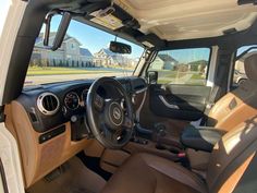 the interior of a vehicle with brown leather seats and steering wheel, in front of a house