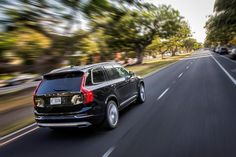 a black suv driving down the road with trees in the backgrouund and cars on both sides