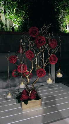 there is a small tree with red roses in the center and two candles on each side