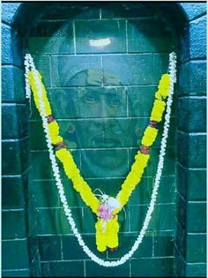 a man's face is covered in flowers and garlands as he stands next to a brick wall