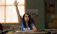 a woman sitting at a desk with her hand up in the air while reading a book