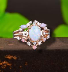 an opal and diamond ring sits on top of a wooden surface with leaves in the background