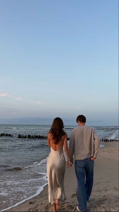 a man and woman walking on the beach holding hands