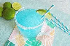 a blue drink with limes and two straws next to it on a napkin