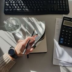 a person writing on a notebook next to a calculator and keyboard