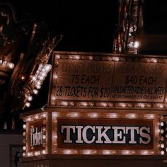 a lighted ticket booth sign in front of a building with lots of lights on it