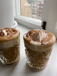 two cups filled with hot chocolate sitting on top of a counter next to a window