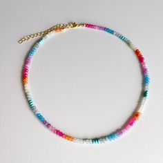 a multicolored beaded necklace on a white surface with a gold plated chain