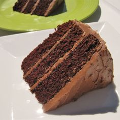 a slice of chocolate cake sitting on top of a white plate next to a green plate