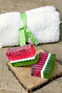 two pieces of watermelon soap sitting on top of a piece of wood next to a towel