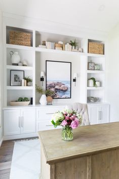 a vase with flowers on top of a wooden table in front of white bookcases