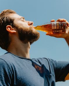 a man drinking from a beer bottle while wearing a blue t - shirt and looking up into the sky