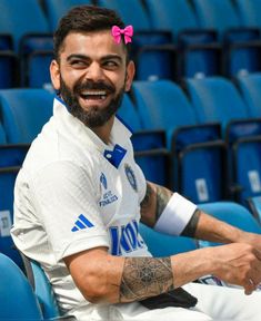 a man with a pink bow in his hair sitting on a blue stadium chair smiling