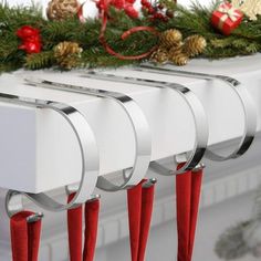 three christmas stockings hang from the mantle with red ribbon and pine cones on it, along with evergreen branches