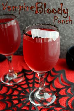 two glasses filled with vampire blood punch sitting on a red tablecloth next to a black and white spider web