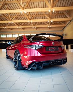 the rear end of a red sports car in a showroom with white tile flooring