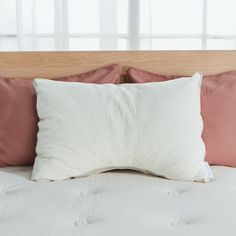 a white pillow on top of a bed with pink and brown pillows next to it