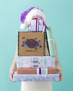 a woman is holding several wrapped presents in her hands and wearing a santa claus hat