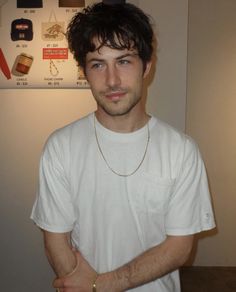 a young man standing in front of a refrigerator wearing a white shirt and gold necklace