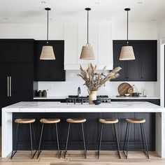 a kitchen with black cabinets and stools in the center, white countertops and wooden flooring