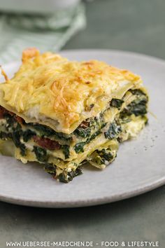 a white plate topped with lasagna covered in cheese and spinach on top of a table