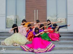 a group of women in colorful dresses sitting on the steps with their arms stretched out