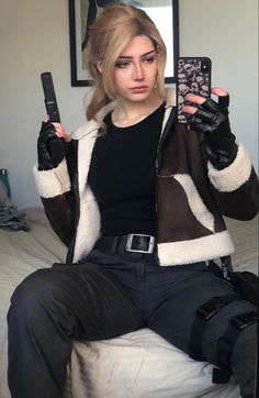 a woman sitting on top of a bed holding two cell phones in one hand and a camera in the other