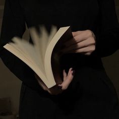 a woman is holding an open book in her hands while wearing a black dress and white nails