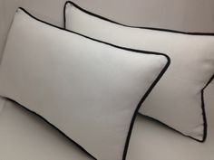 two white pillows with black piping on the edges are sitting next to each other