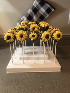 sunflower cake pops are arranged on a white stand with black and white checkered napkin