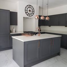 a kitchen with black cabinets and white counter tops, an island in the middle has copper accents