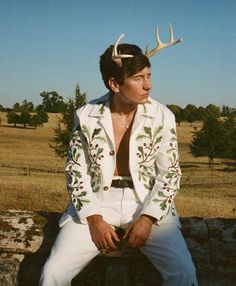 a man with antlers on his head sitting on a rock in front of a field