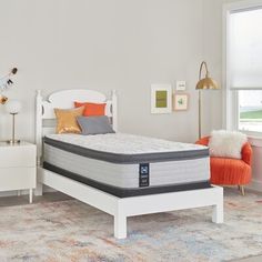 a bedroom with a white bed, orange and blue pillows, and an area rug on the floor