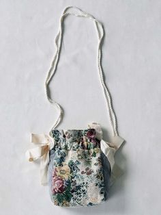 a flowered purse hanging from a white string on a wall with a bow at the top