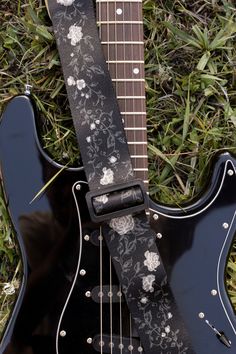 a black guitar strap with white flowers on it sitting next to an electric guitar in the grass