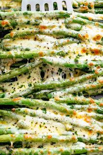 asparagus covered in cheese and parmesan on a baking sheet with a spatula